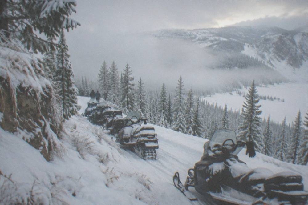 A line of snowmobiles parked beside a snowy trail winding through frozen forest