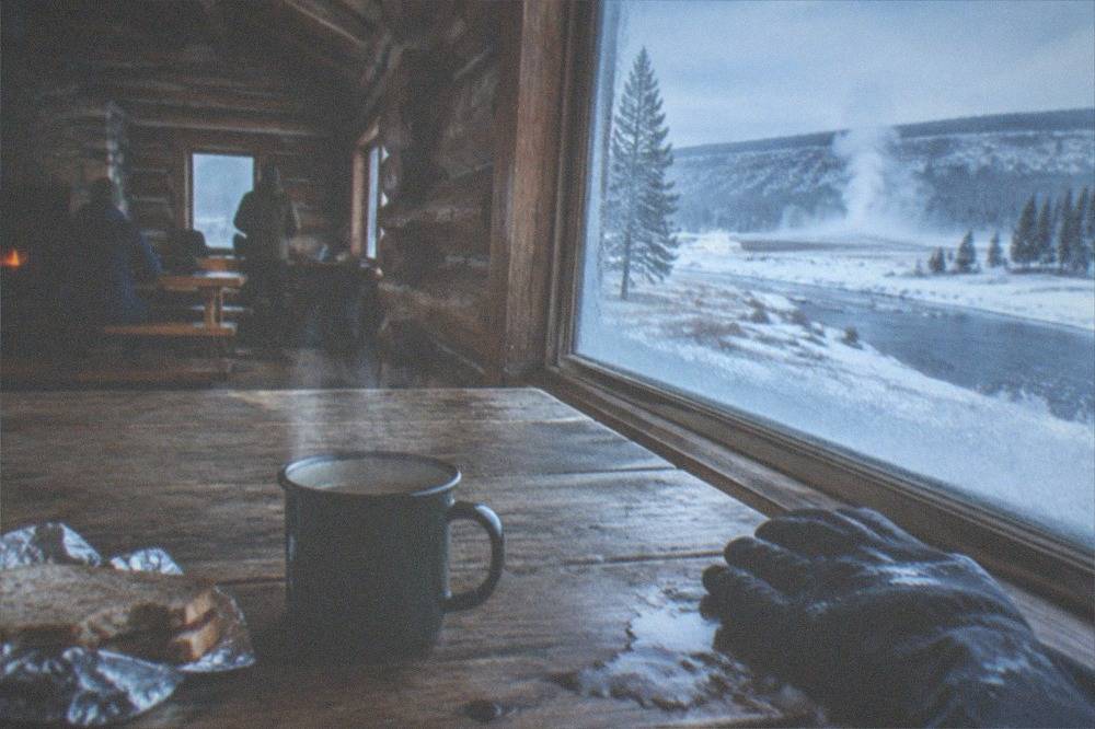 A steaming mug and packed lunch laid out on a wooden table inside a warm park warming hut.