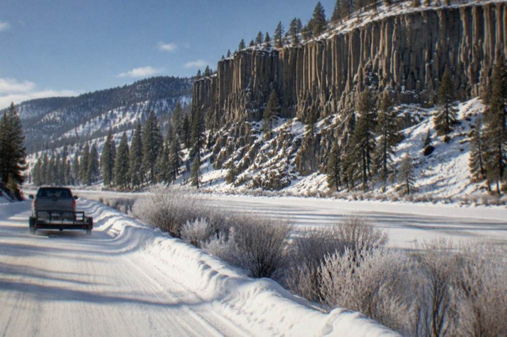Snow-packed road following a frozen river through a mountain valley in winter
