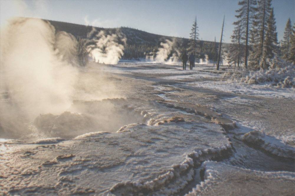 Steam rising from a snow-covered geyser basin under a clear winter sky