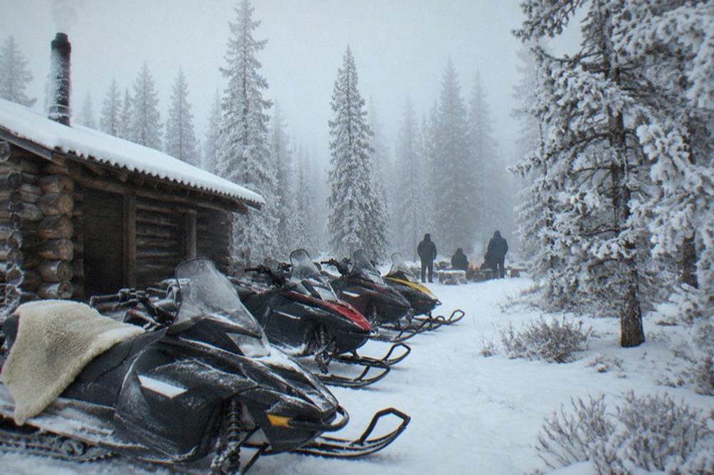 Snowmobiles parked in a row beside a wooden warming hut at the edge of a snowy forest clearing