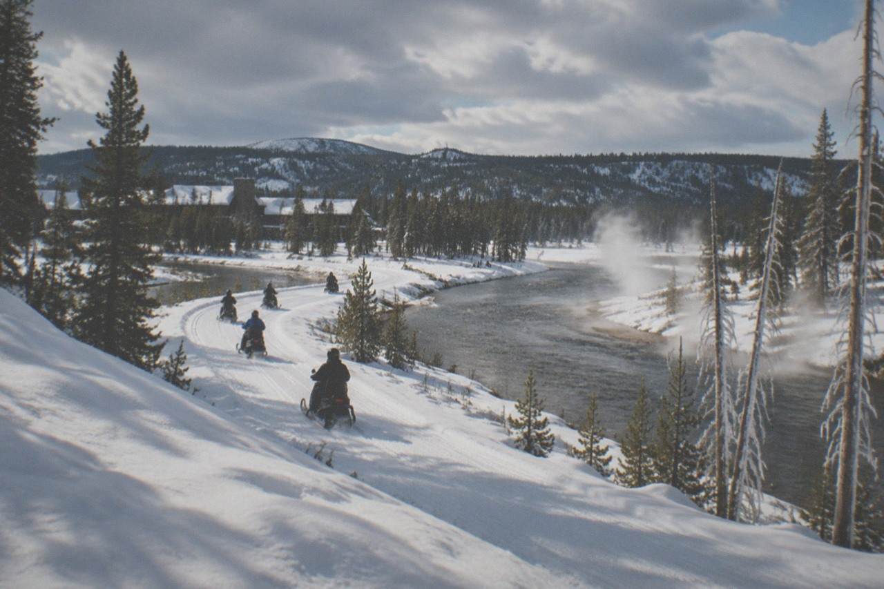 A line of snowmobiles traveling a groomed snow road through a snowy Yellowstone landscape