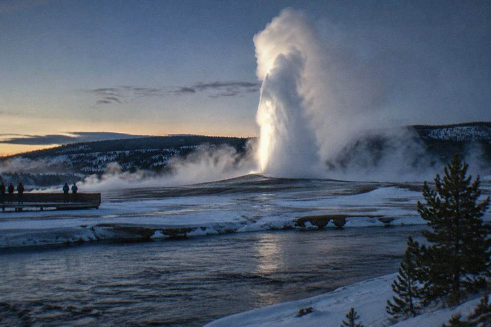 A geyser erupting steam into cold air above deep snow