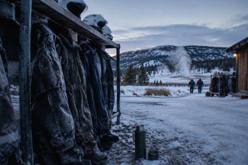 Insulated snowmobile suits and helmets lined up on a rack at a winter tour staging area