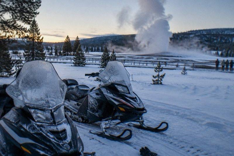 Snowmobiles at Old Faithful geyser basin with steam rising over fresh snow