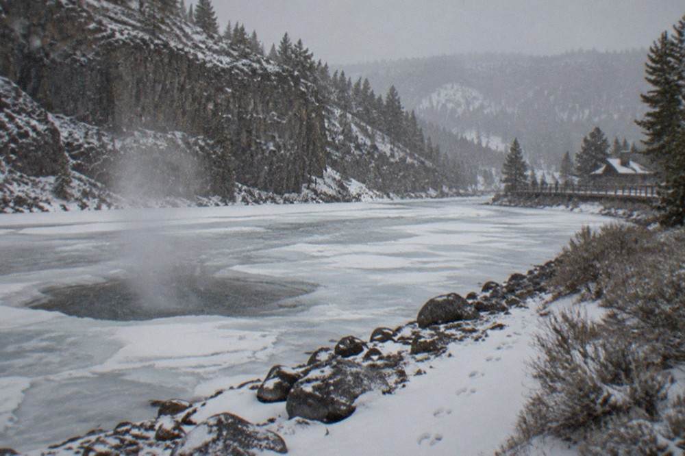 Snow-covered mountain road winding along a frozen river valley toward high forested peaks