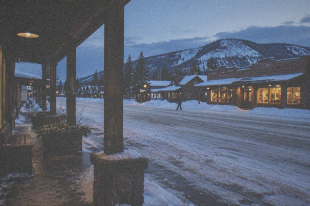 Small western town main street in winter with snow banks and warm shop lights at dusk