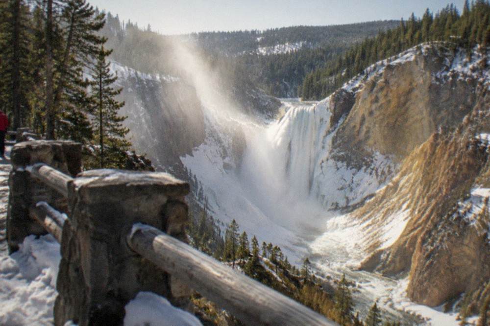 A deep snowy canyon with a partly frozen waterfall and golden rock walls under a clear winter sky