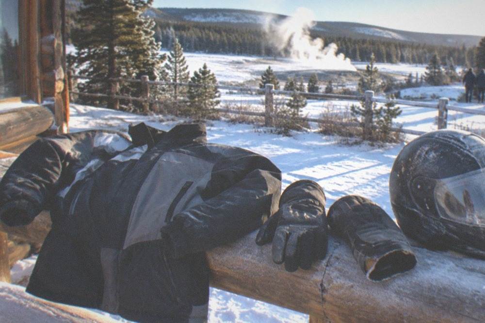 An insulated snowmobile suit jacket and gloves laid out on a wooden bench beside a helmet
