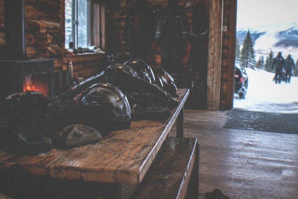 A stack of insulated jackets, gloves, boots and helmets arranged on a bench inside a warm wooden lodge