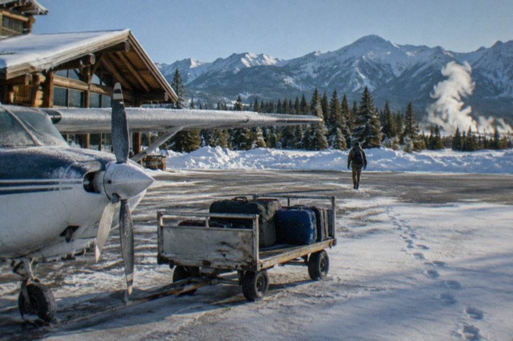 A small regional airport terminal with snow banks along the runway and mountains behind