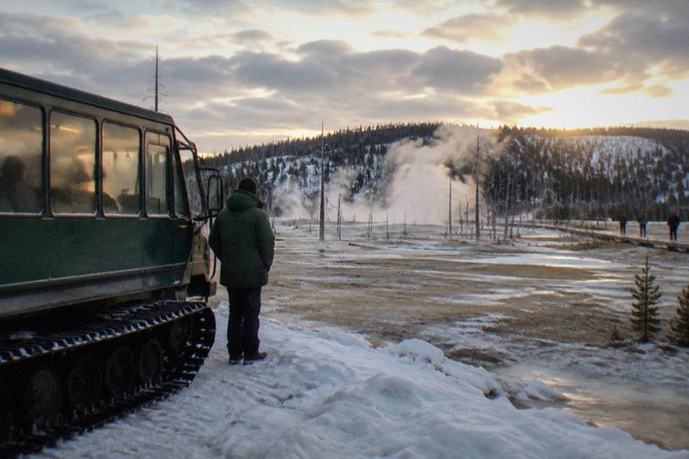 A heated snowcoach parked on a snowy road with a guide standing beside it
