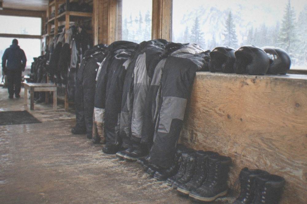 Insulated snowmobile suits, helmets and boots laid out on a bench inside a rental outfitter