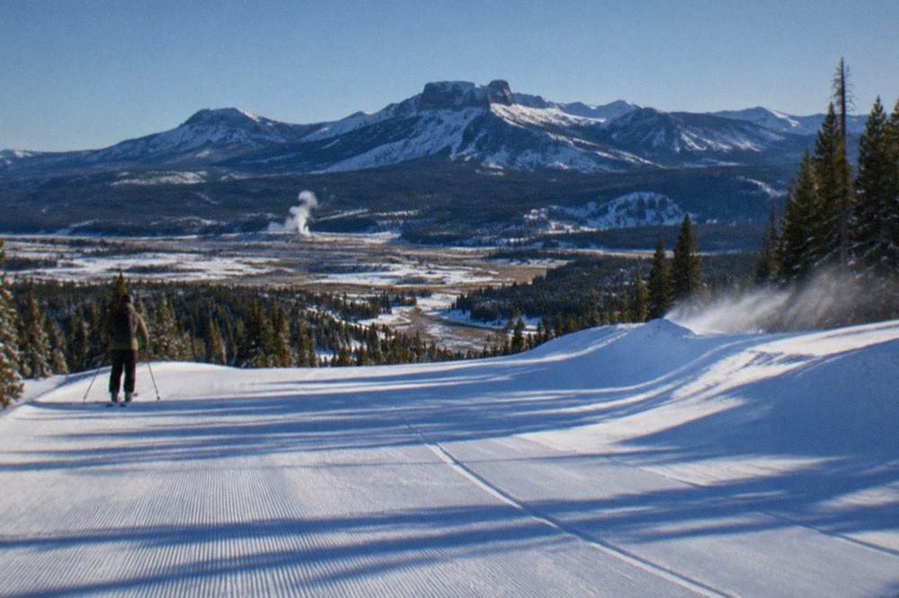 Snow-covered groomed snowmobile trail with distant mountains under a clear winter sky