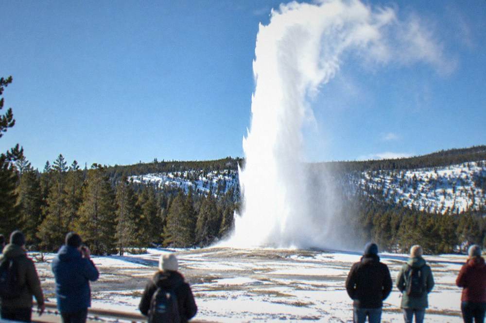 Old Faithful geyser erupting into cold air above a snow-covered basin