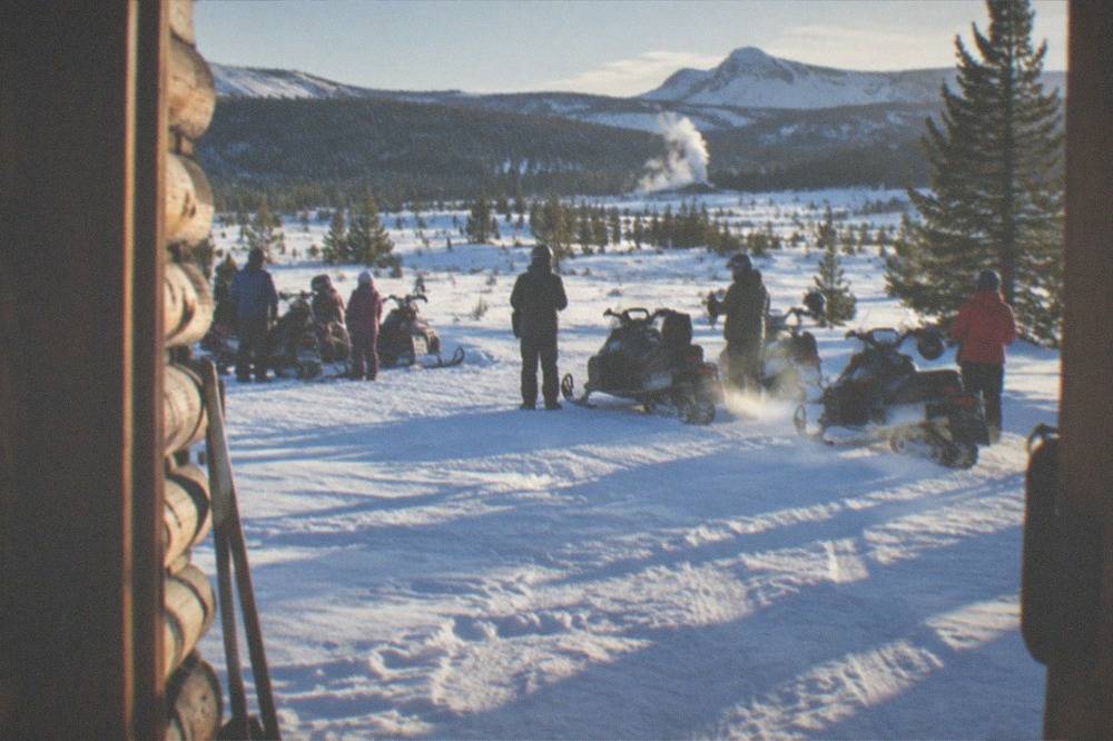 Families gathered around snowmobiles at a forest trailhead in deep snow