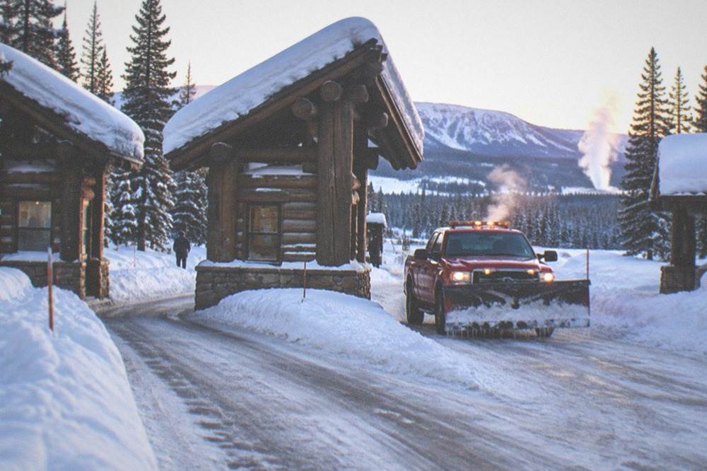 Winter park entrance sign with snow banks along a plowed road at dawn
